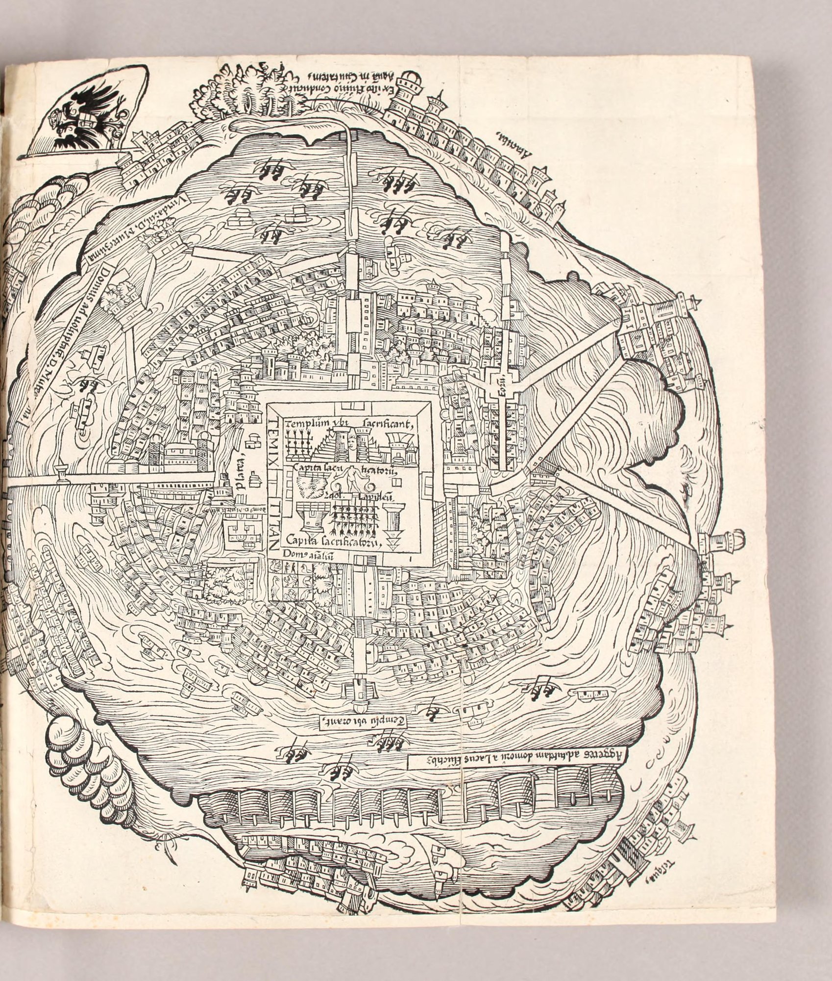 A round island city in a lake, seen from above. Causeways lead out to towns on the shore. In the center a walled square holds a stepped temple, racks of skulls and a statue. Houses crowd the island, canoes cross the water, and an imperial eagle banner flies at upper left.